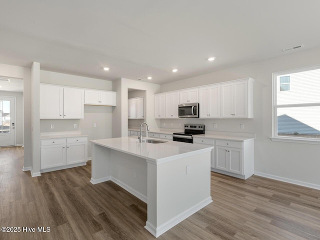 kitchen with stainless steel appliances, a healthy amount of sunlight, white cabinets, and a kitchen island with sink