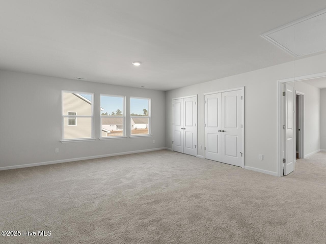 unfurnished bedroom featuring light carpet and multiple closets