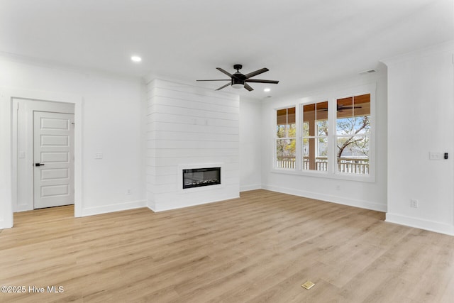 unfurnished living room with crown molding, a large fireplace, ceiling fan, and light hardwood / wood-style flooring