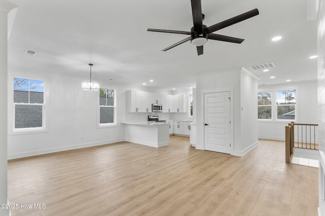 unfurnished living room featuring a wealth of natural light, light hardwood / wood-style flooring, and ceiling fan with notable chandelier