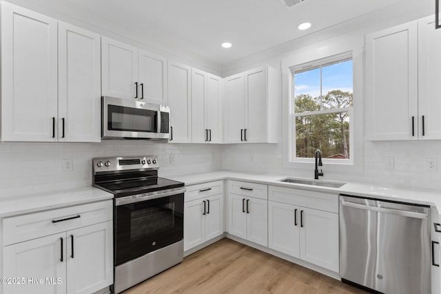 kitchen featuring sink, appliances with stainless steel finishes, white cabinetry, tasteful backsplash, and light hardwood / wood-style floors