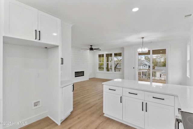 kitchen featuring white cabinetry, light hardwood / wood-style flooring, a large fireplace, pendant lighting, and ceiling fan with notable chandelier