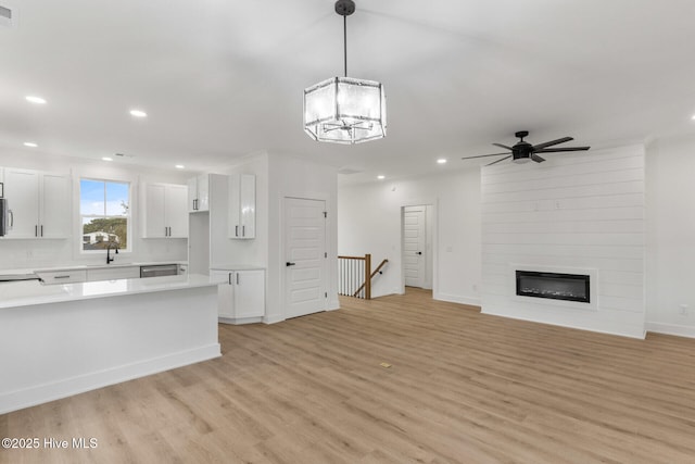 unfurnished living room with sink, ceiling fan with notable chandelier, a fireplace, and light hardwood / wood-style floors