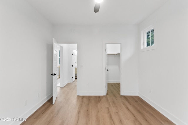 unfurnished bedroom with ceiling fan, a spacious closet, a closet, and light hardwood / wood-style flooring