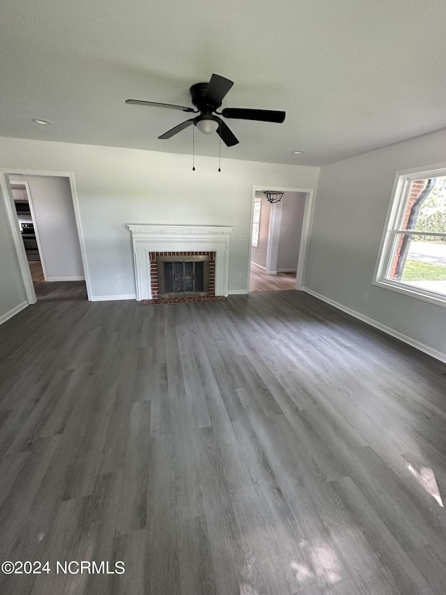 unfurnished living room with a brick fireplace, dark wood finished floors, baseboards, and ceiling fan