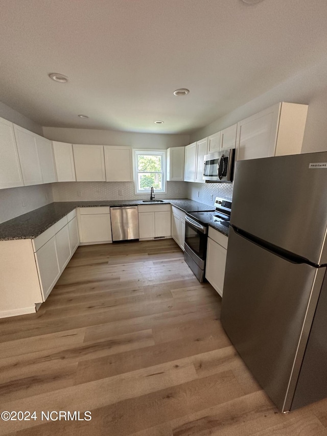 kitchen with light wood finished floors, decorative backsplash, white cabinets, appliances with stainless steel finishes, and a sink