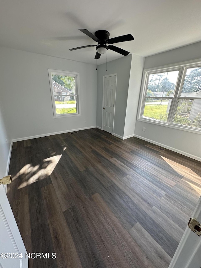 spare room featuring dark wood-style flooring, plenty of natural light, visible vents, and baseboards