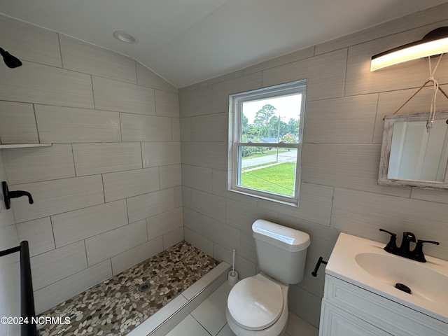 bathroom featuring lofted ceiling, toilet, a tile shower, vanity, and tile walls