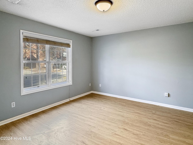 unfurnished room with light wood-type flooring and a textured ceiling