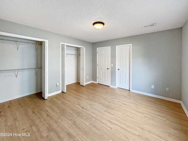 unfurnished bedroom featuring two closets, a textured ceiling, and light hardwood / wood-style floors