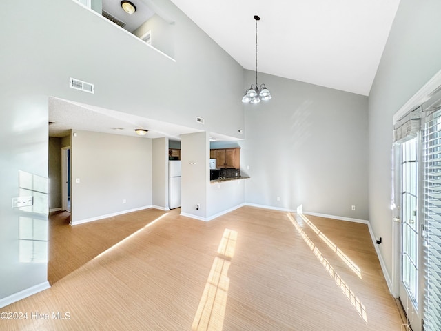 unfurnished living room with a chandelier, light wood-type flooring, and high vaulted ceiling