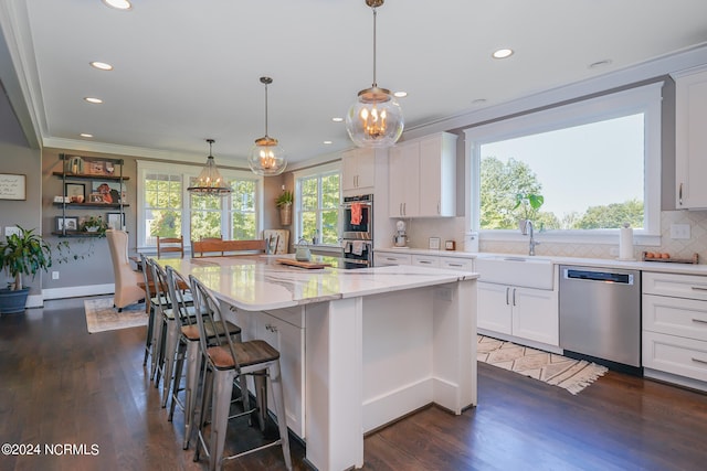 kitchen with light stone counters, stainless steel appliances, pendant lighting, white cabinets, and a center island