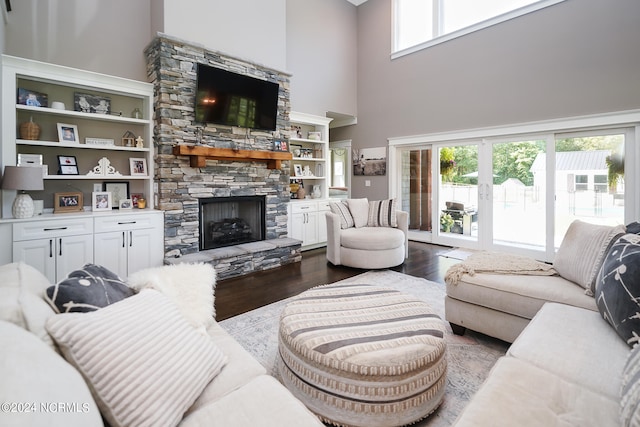 living room featuring a high ceiling, dark hardwood / wood-style flooring, a stone fireplace, and built in shelves