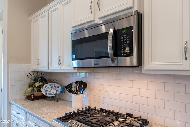 kitchen featuring white cabinets, decorative backsplash, stainless steel appliances, and light stone countertops