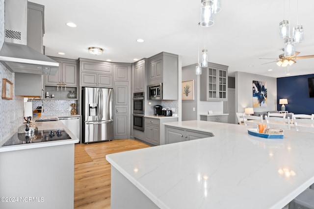 kitchen with appliances with stainless steel finishes, wall chimney range hood, gray cabinets, and backsplash