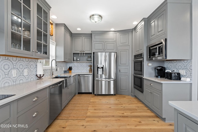 kitchen with appliances with stainless steel finishes, light hardwood / wood-style floors, decorative backsplash, sink, and gray cabinets