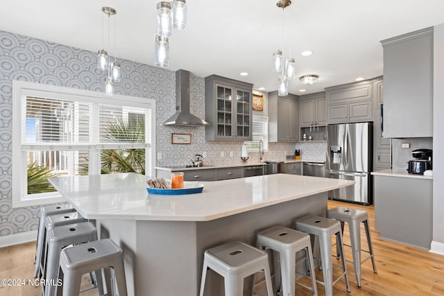 kitchen with a breakfast bar area, stainless steel appliances, wall chimney exhaust hood, and hanging light fixtures