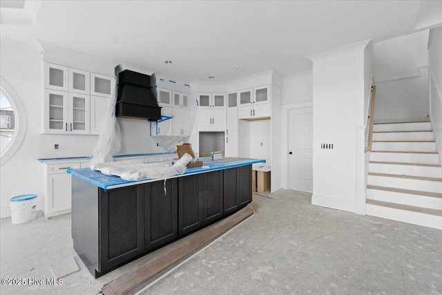 kitchen featuring premium range hood, an island with sink, and white cabinets