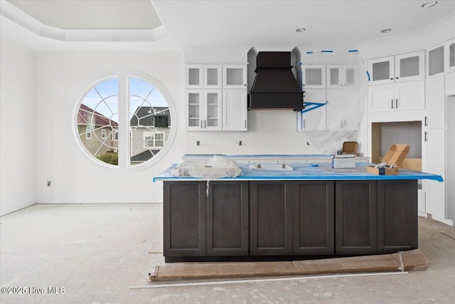 kitchen featuring white cabinetry, premium range hood, dark brown cabinets, and an island with sink