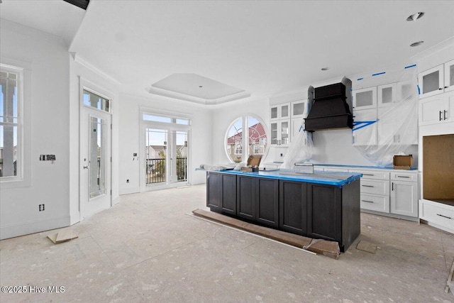 kitchen featuring white cabinetry, custom exhaust hood, a raised ceiling, and a kitchen island