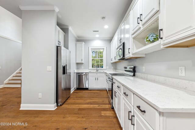 kitchen featuring light stone counters, white cabinets, stainless steel appliances, wood-type flooring, and ornamental molding