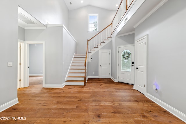 foyer with light wood-type flooring, ornamental molding, and high vaulted ceiling