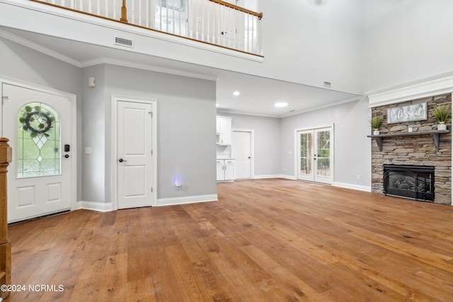 unfurnished living room with a stone fireplace, light hardwood / wood-style flooring, a towering ceiling, and ornamental molding