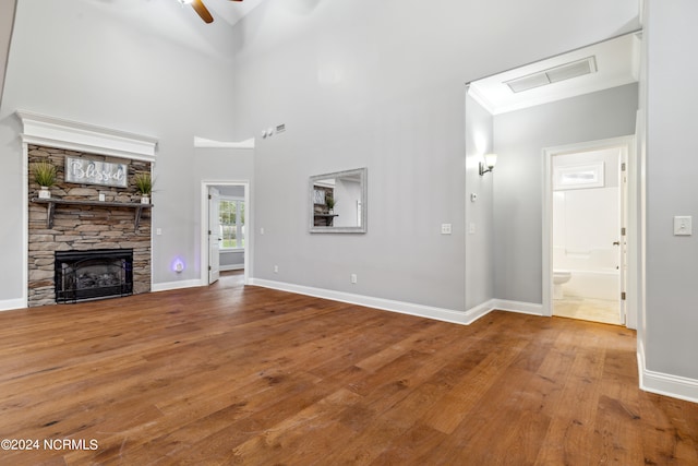 unfurnished living room with a high ceiling, wood-type flooring, a fireplace, and ceiling fan