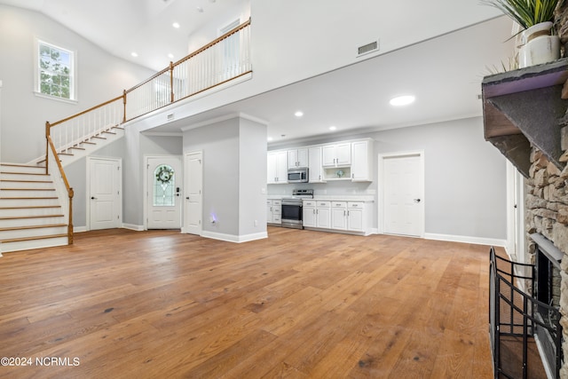 unfurnished living room featuring high vaulted ceiling, a stone fireplace, light hardwood / wood-style flooring, and a wealth of natural light