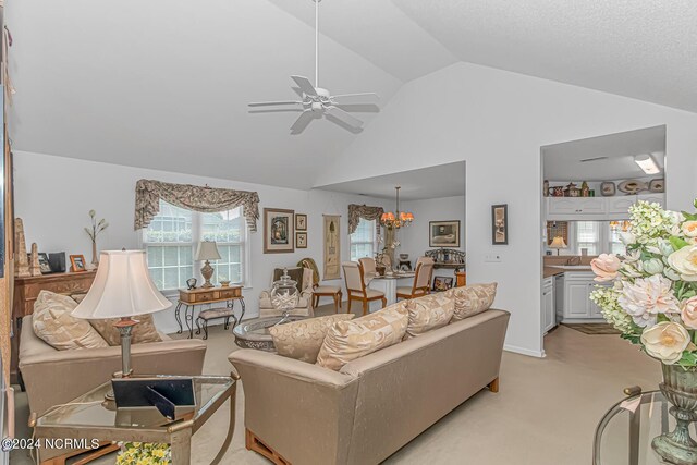 living room featuring high vaulted ceiling, ceiling fan with notable chandelier, and light colored carpet