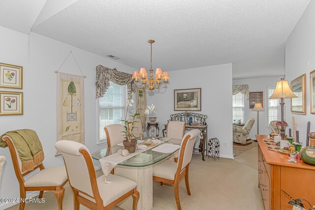 dining room with a textured ceiling, a healthy amount of sunlight, an inviting chandelier, and light colored carpet