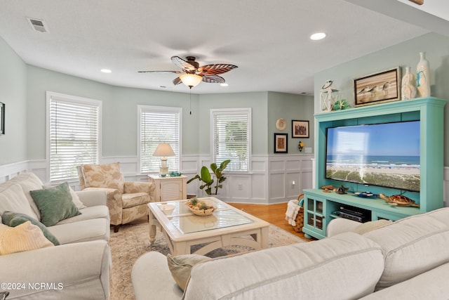 living room featuring light wood-style floors, a ceiling fan, visible vents, and a wealth of natural light