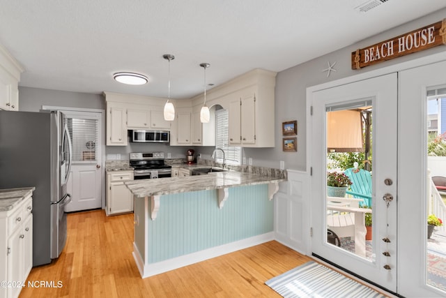 kitchen featuring appliances with stainless steel finishes, a peninsula, french doors, light wood-type flooring, and a sink