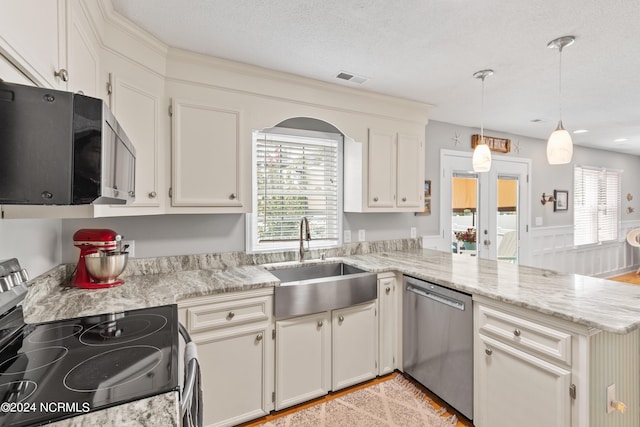 kitchen featuring decorative light fixtures, stainless steel appliances, visible vents, a sink, and a peninsula