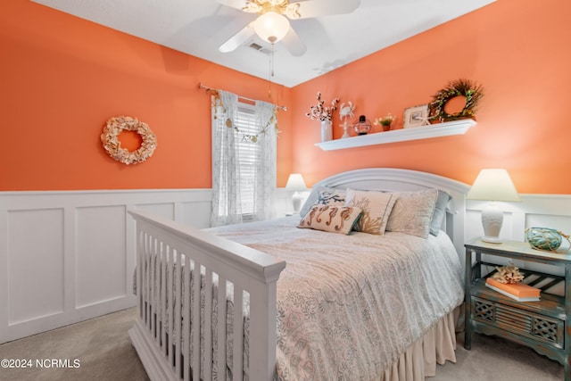 bedroom with visible vents, a decorative wall, wainscoting, carpet flooring, and ceiling fan