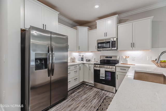 kitchen with hardwood / wood-style flooring, crown molding, appliances with stainless steel finishes, white cabinetry, and decorative backsplash