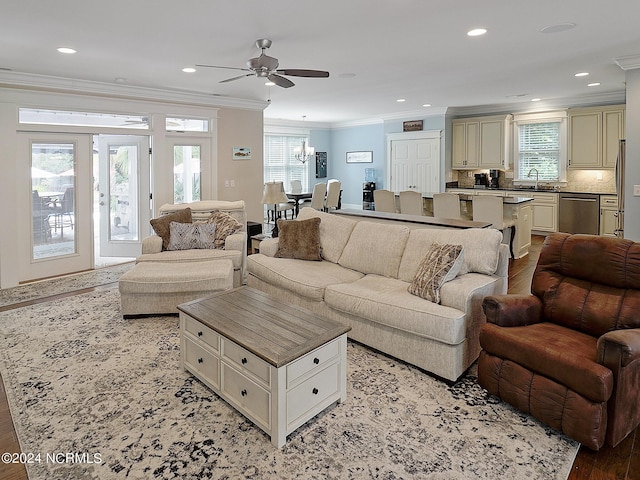 living room featuring ceiling fan with notable chandelier, light hardwood / wood-style flooring, crown molding, and sink