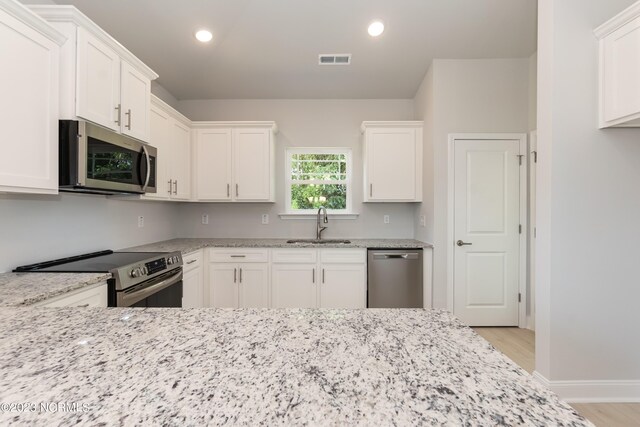 kitchen with stainless steel appliances, white cabinetry, and light wood-type flooring