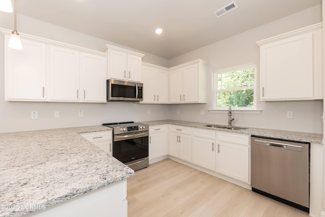 kitchen with stainless steel appliances, sink, light wood-type flooring, white cabinets, and hanging light fixtures