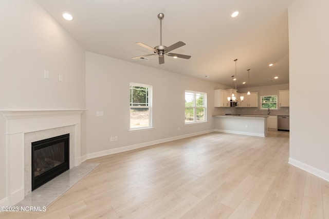 unfurnished living room featuring light wood-type flooring, ceiling fan with notable chandelier, and a high end fireplace