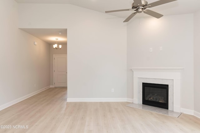 unfurnished living room with light wood-type flooring, ceiling fan with notable chandelier, a premium fireplace, and lofted ceiling