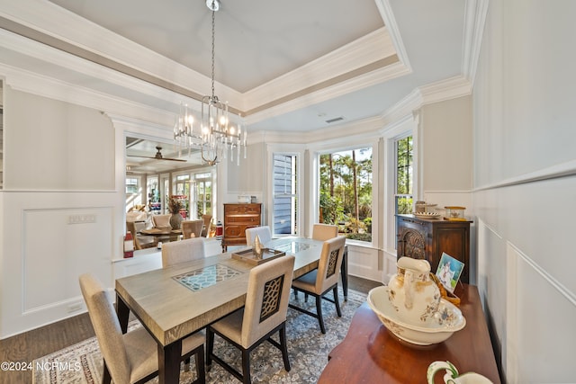 dining space featuring a raised ceiling, ornamental molding, dark wood-style flooring, an inviting chandelier, and a decorative wall