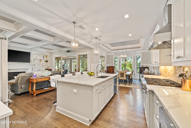 kitchen featuring a center island with sink, hanging light fixtures, range hood, white cabinetry, and a sink