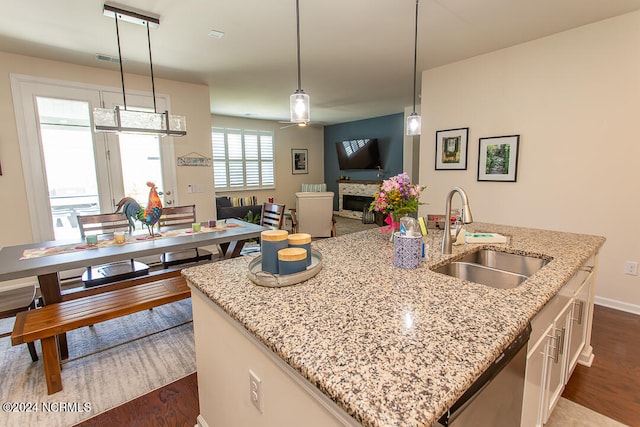 kitchen featuring dark hardwood / wood-style flooring, hanging light fixtures, a kitchen island with sink, light stone countertops, and sink