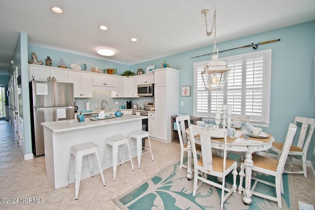 kitchen featuring tasteful backsplash, white cabinets, a kitchen island, appliances with stainless steel finishes, and a kitchen breakfast bar