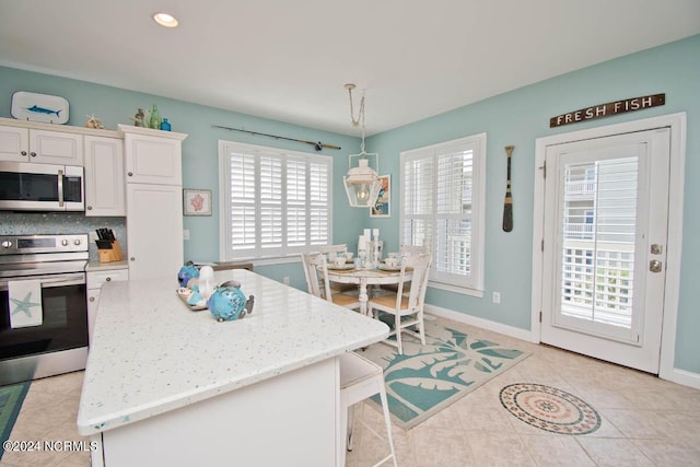 kitchen with appliances with stainless steel finishes, tasteful backsplash, white cabinetry, hanging light fixtures, and light tile patterned flooring