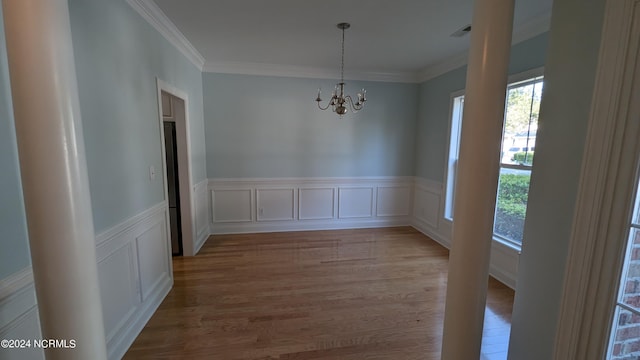 unfurnished dining area featuring an inviting chandelier, visible vents, ornamental molding, and wood finished floors