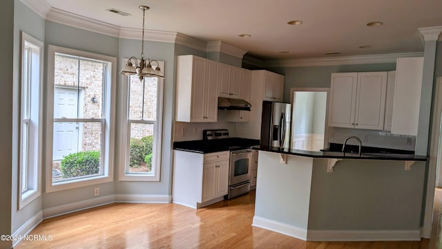 kitchen with appliances with stainless steel finishes, dark countertops, a kitchen bar, and under cabinet range hood