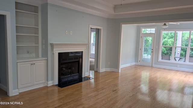 unfurnished living room featuring built in shelves, light hardwood / wood-style flooring, ceiling fan, and crown molding