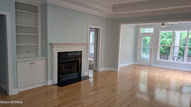 unfurnished living room with built in shelves, light wood finished floors, a ceiling fan, ornamental molding, and a fireplace with flush hearth